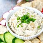 bowl of caramelized onion dip with crackers and sliced cucumbers.