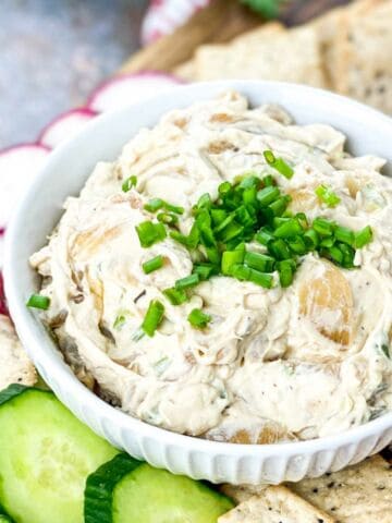 bowl of caramelized onion dip with crackers and sliced cucumbers.