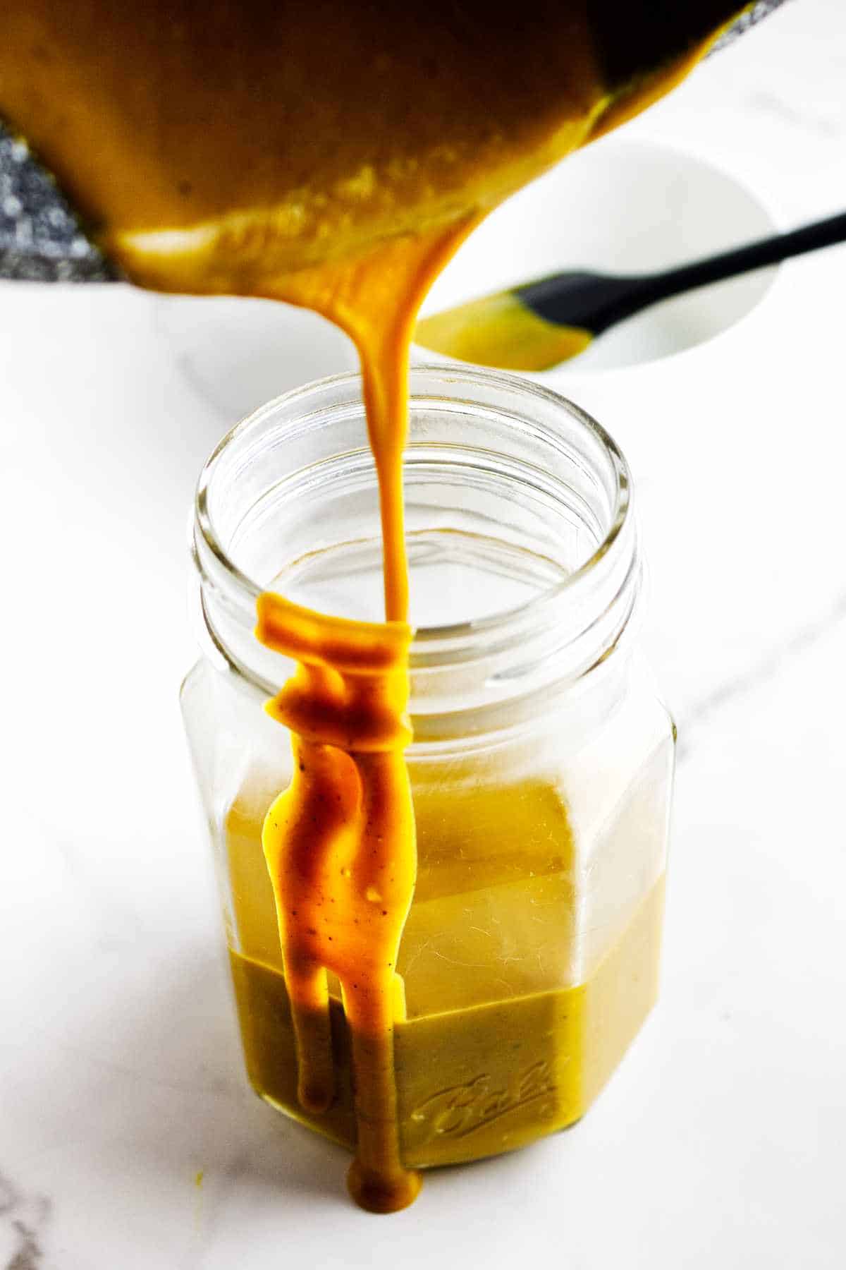 pouring gold barbeque sauce into a Mason jar.