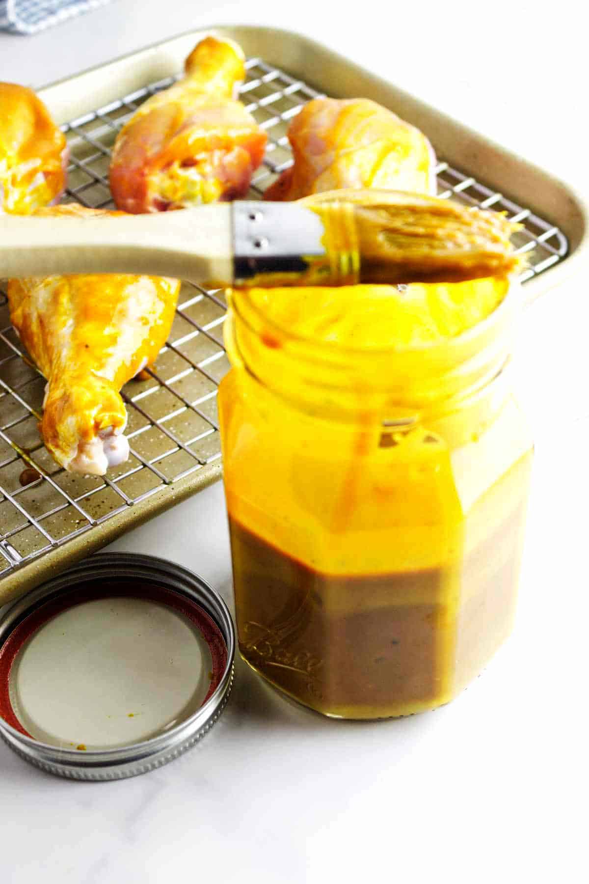 basting brush with gold bbq sauce near a rack of barbecue basted chicken drumsticks.