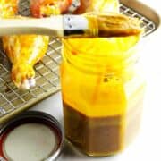 basting brush with gold bbq sauce near a rack of barbecue basted chicken drumsticks.