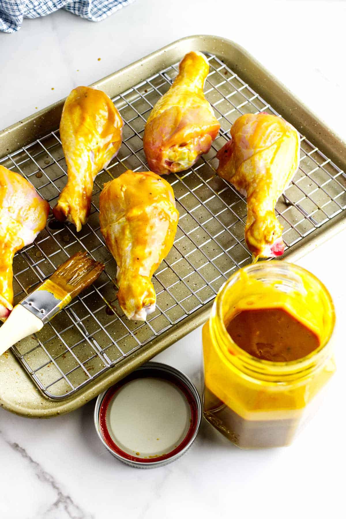 basting brush with mustard sauce near a rack of barbecue basted chicken drumsticks.