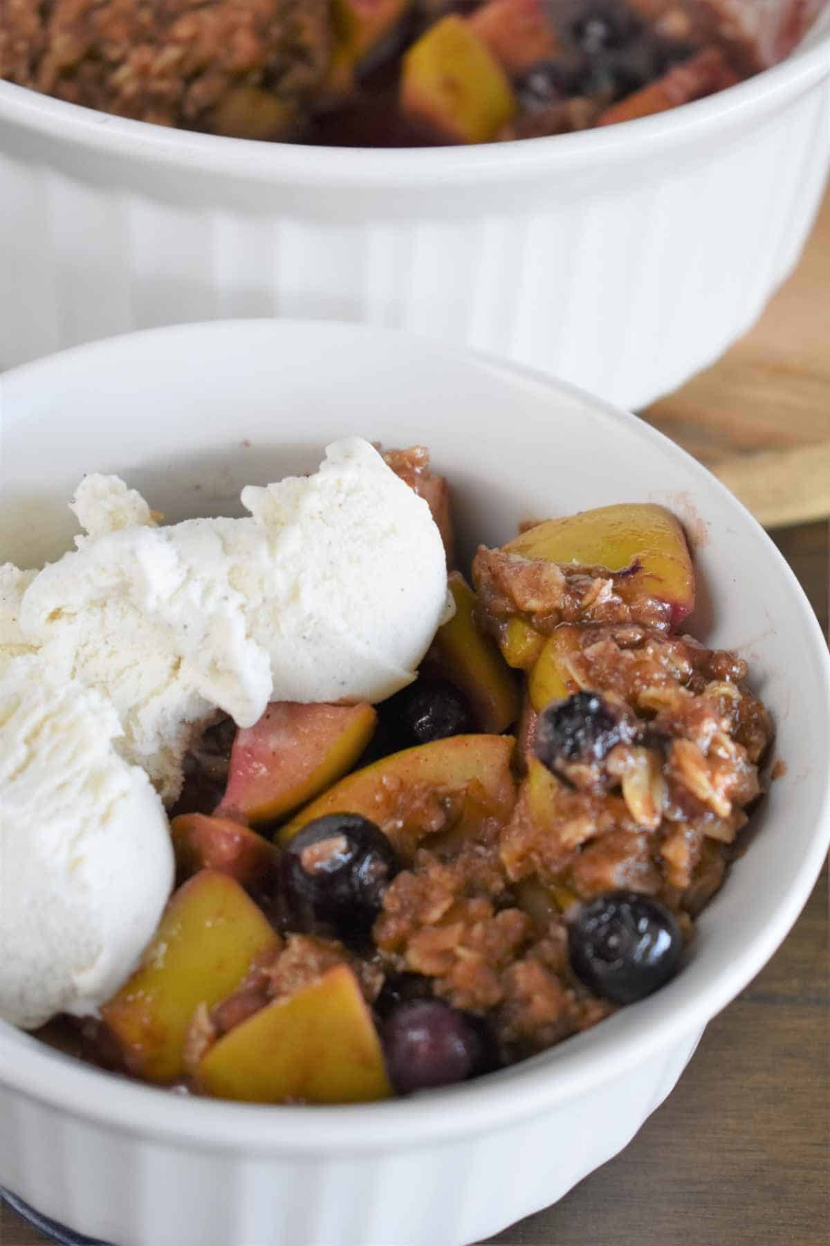 serving dish with scoops of apple blueberry cobbler topped with vanilla ice cream.