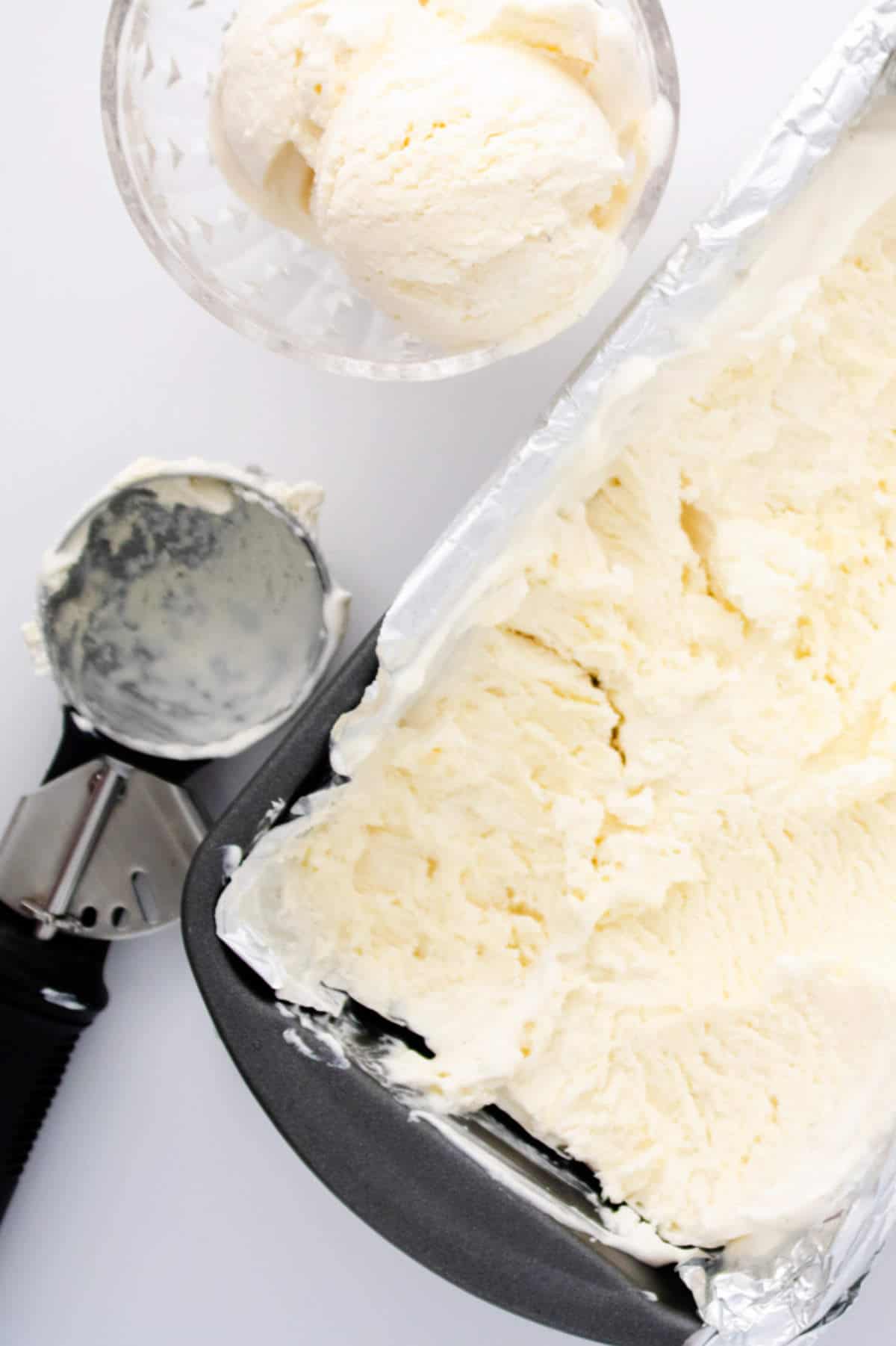 loaf pan of vanilla ice cream, ice cream scoop, and bowl of ice cream.