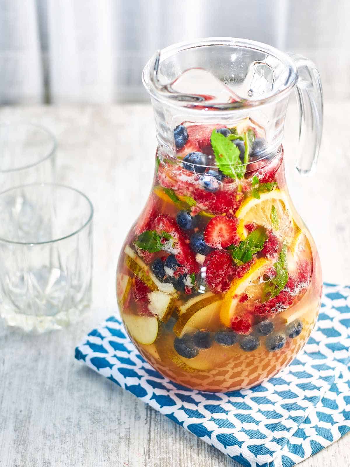 Pitcher of fruits and clear beverage.