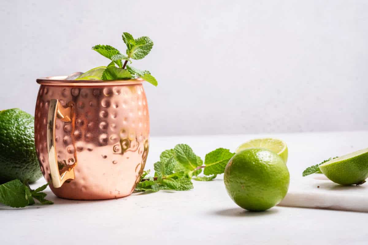 ingredients for ginger beer cocktail in copper mug with lime, mint and cucumber.