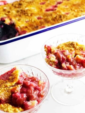 pan of Rhubarb dump cake in the background with servings in two parfait glasses.