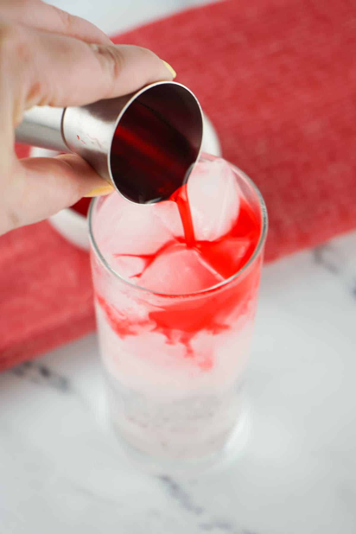 Pouring grenadine syrup into tall glasses.