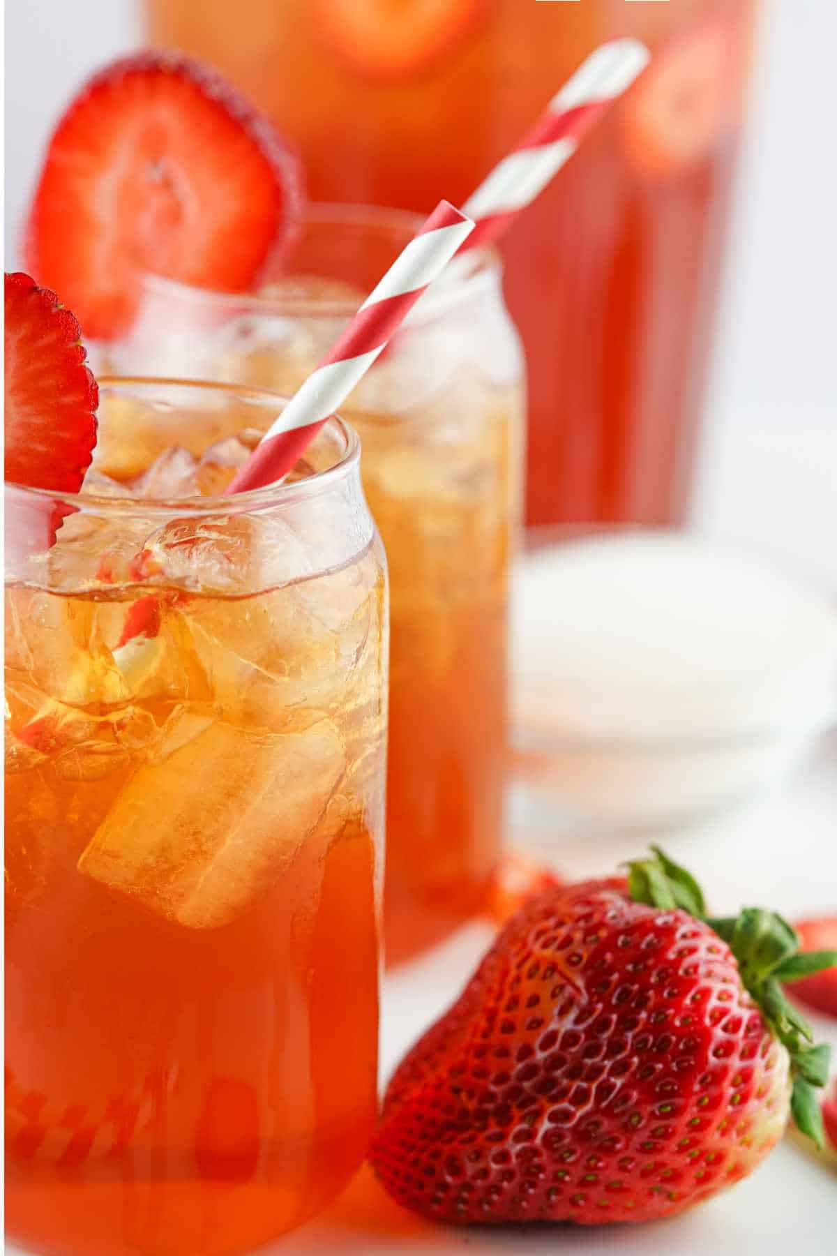 two tall glasses of strawberry Arnold Palmer with straws and strawberry garnish.
