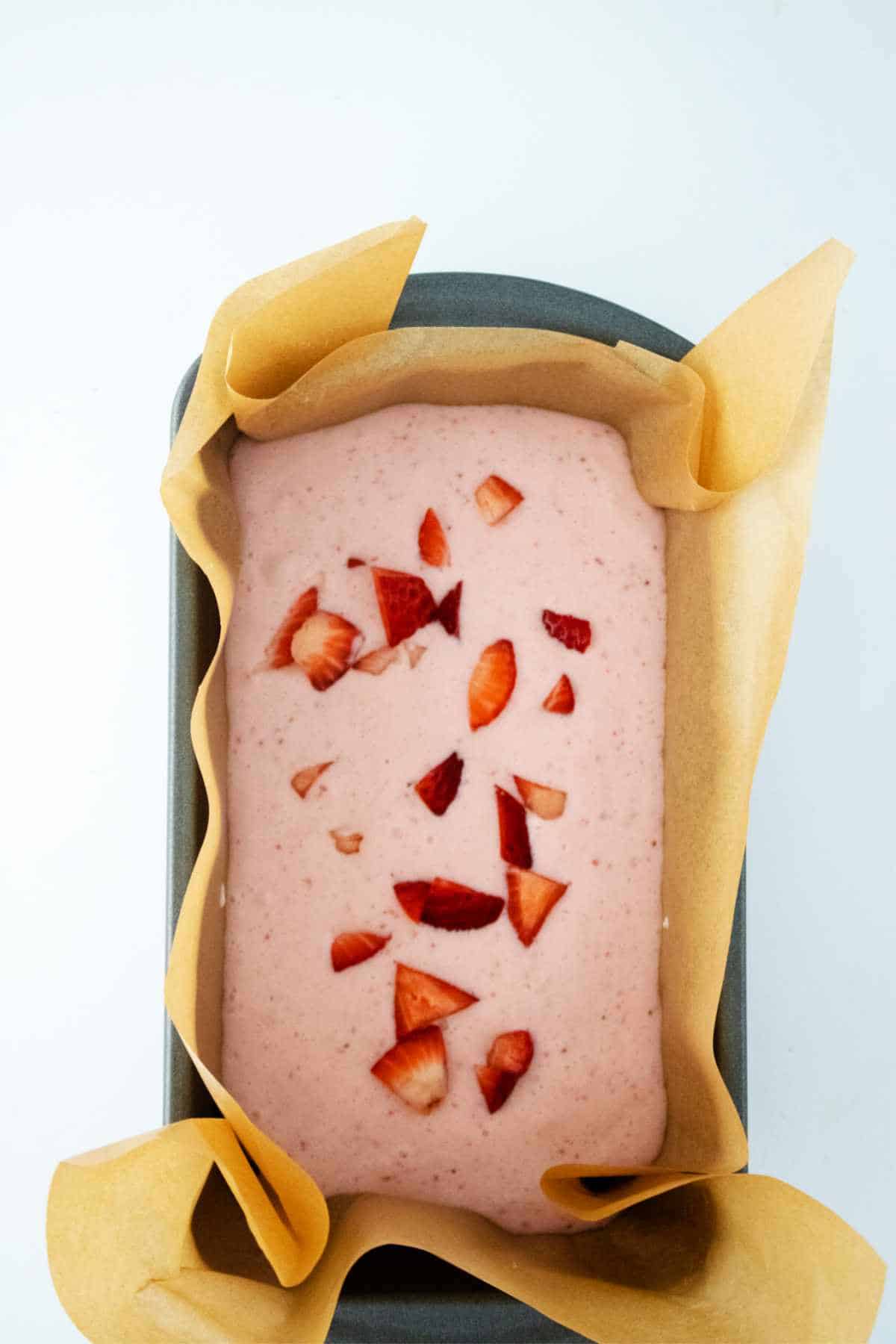 ice cream with cut strawberries on top in a loaf pan.