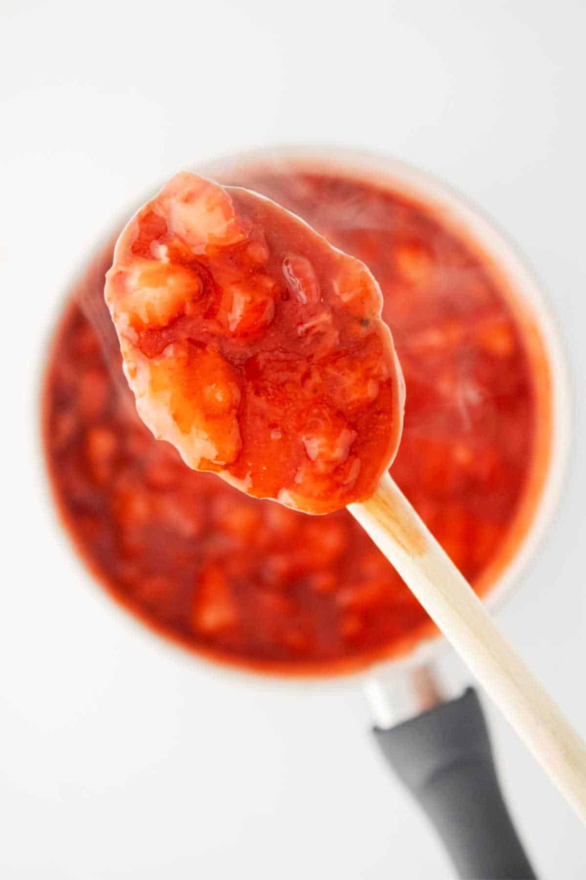 Spoonful of thickened jam above a sauce pan of simmering jam.