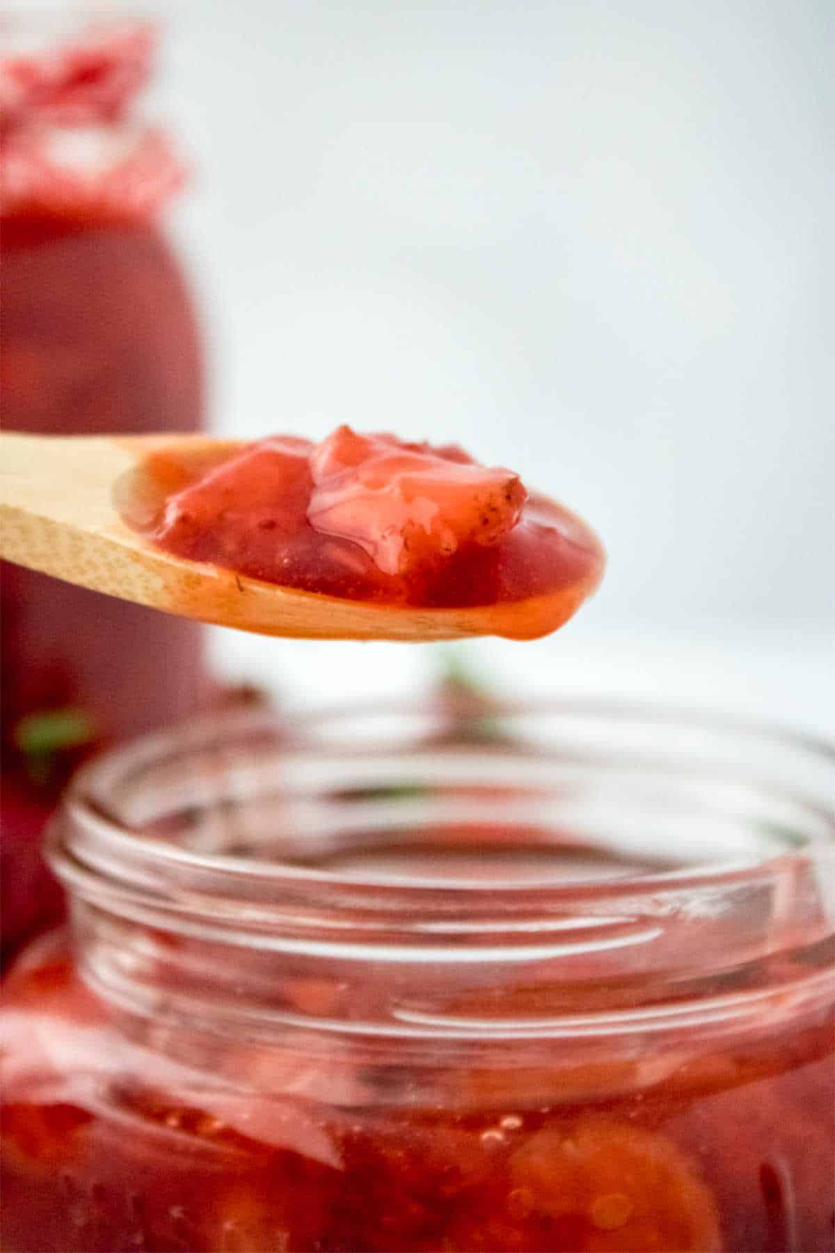Spooning hot strawberry jam into a jar.