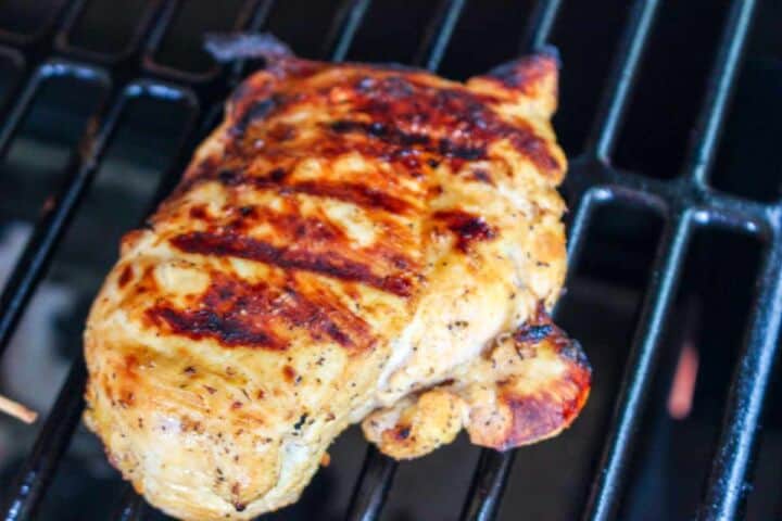 Grilled, seasoned chicken breast with char marks cooks on a black grill grate, similar to Traeger smoked chicken.