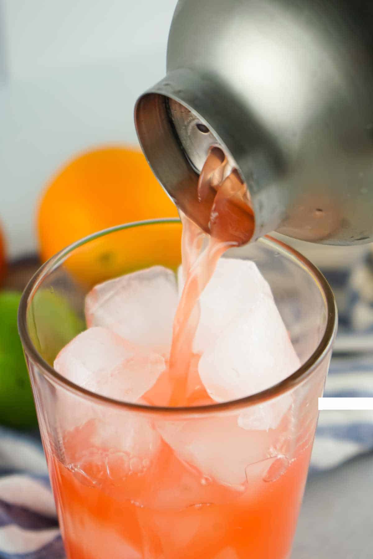 shaker pouring mixed drink into ice filled tumbler.