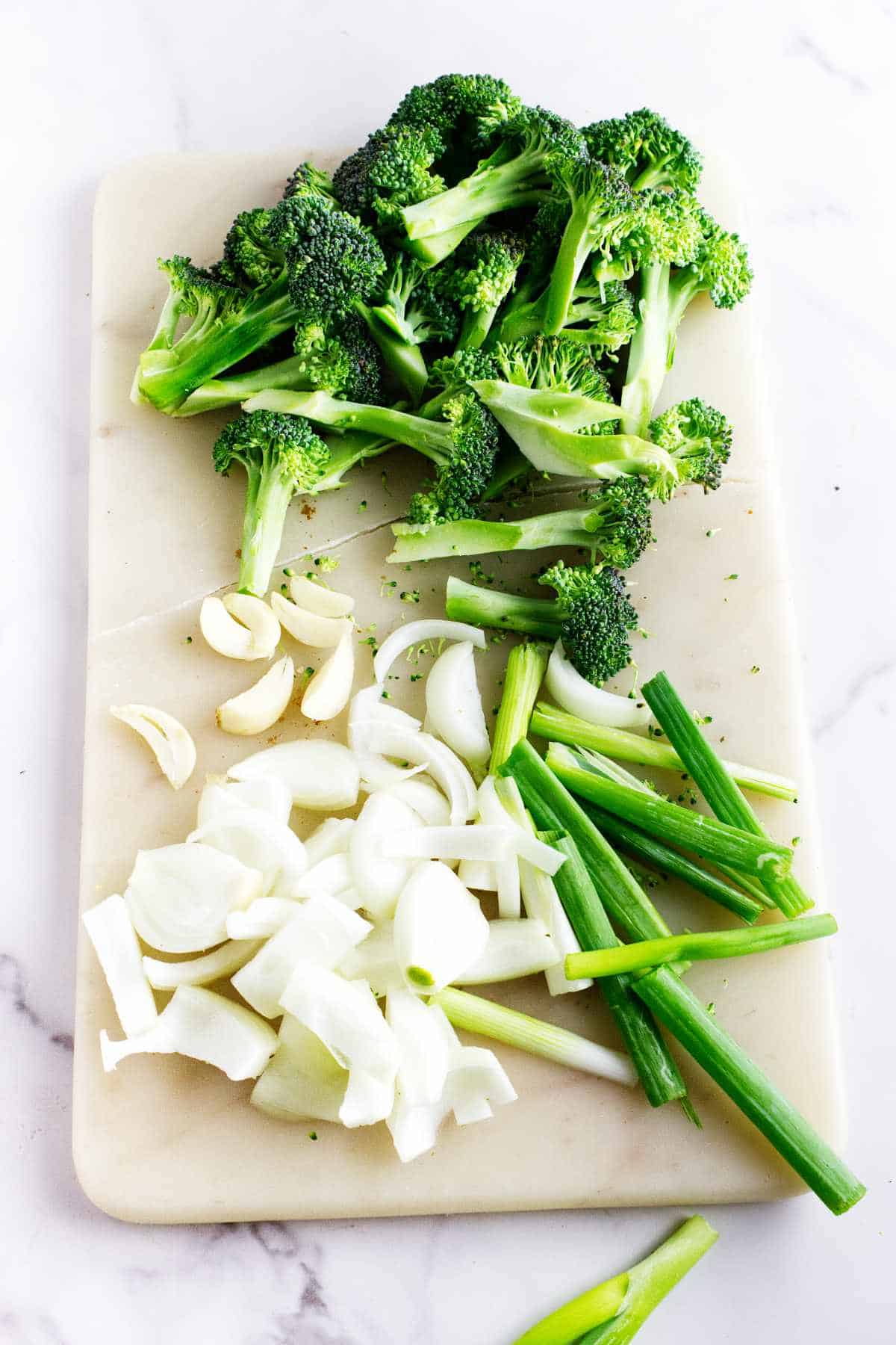 cut onions and broccoli ona white marble cutting board.
