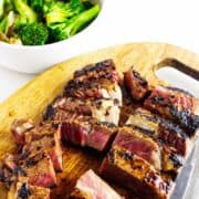 cut Blackstone grilled beef Teppanyaki on a cutting board with a bowl of grilled broccoli in the background.