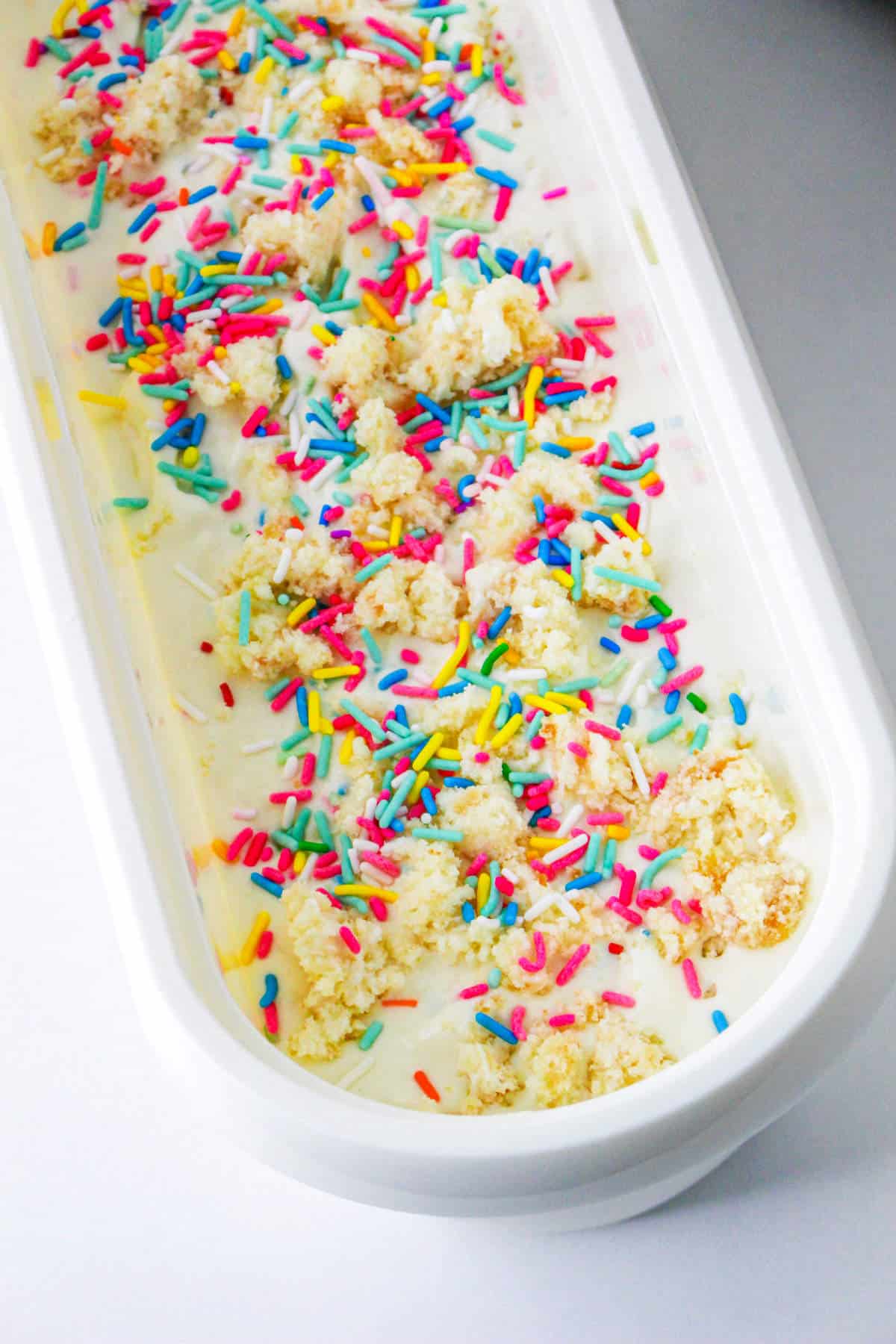 layers of ice cream, crumbled cupcake, and rainbow sprinkles in an ice cream hardening freezer container.