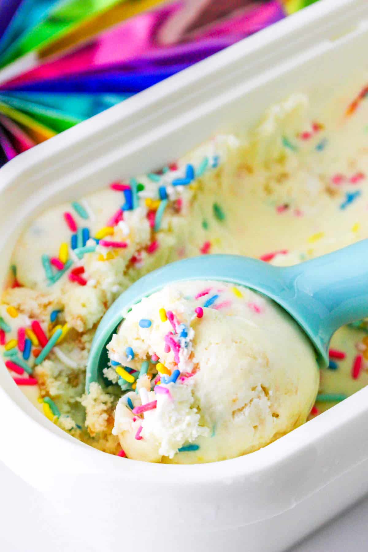 scooping rainbow sprinkles gelato from storage container.