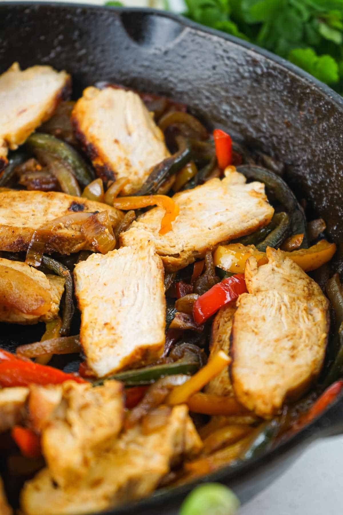 Skillet chicken fajitas with sliced chicken, peppers, and onions in a cast iron pan.