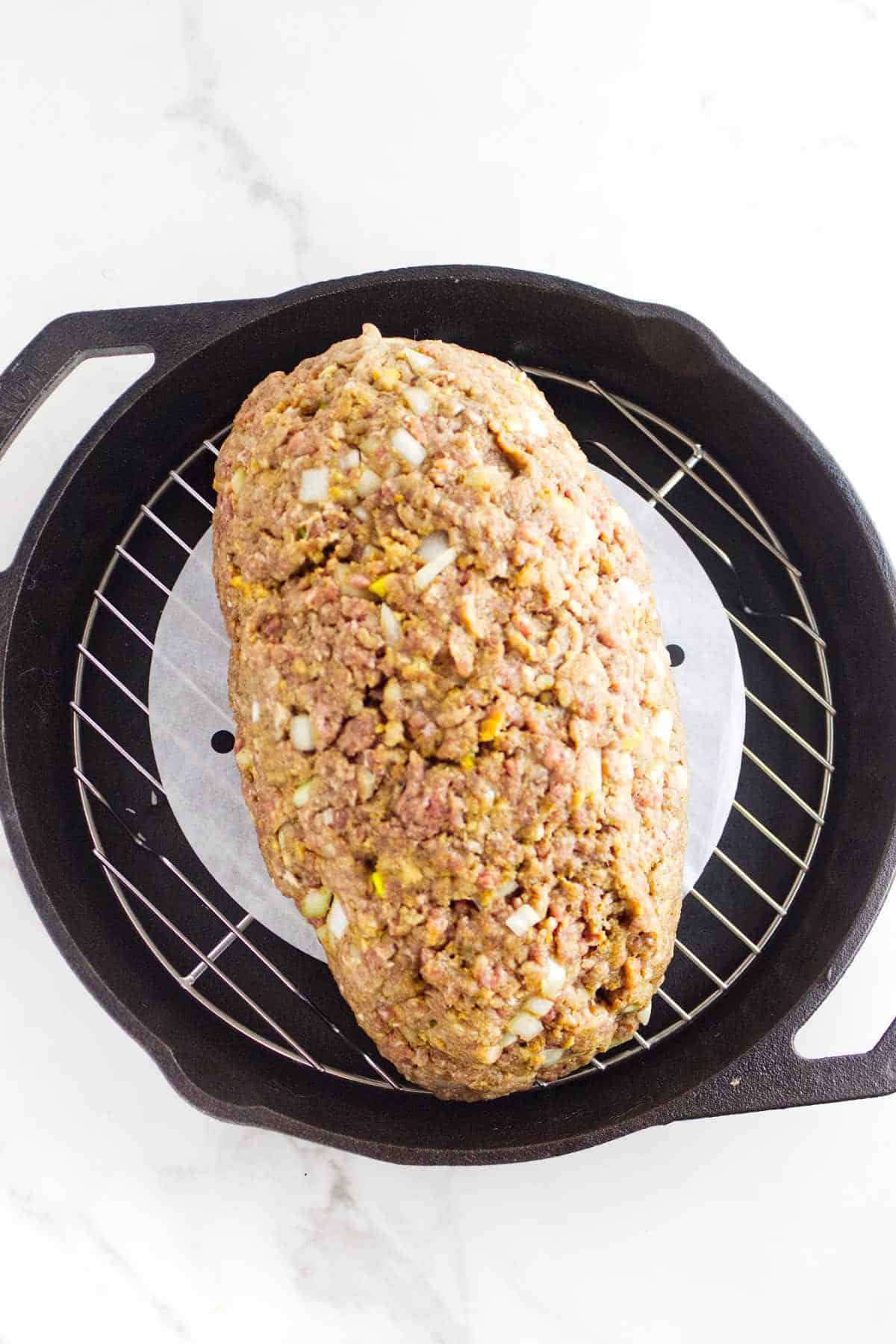 shaped seasoned minced beef on a grilling rack in a cast iron skillet.