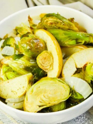 Serving bowl with roasted brussels sprouts and sliced granny smith apples.