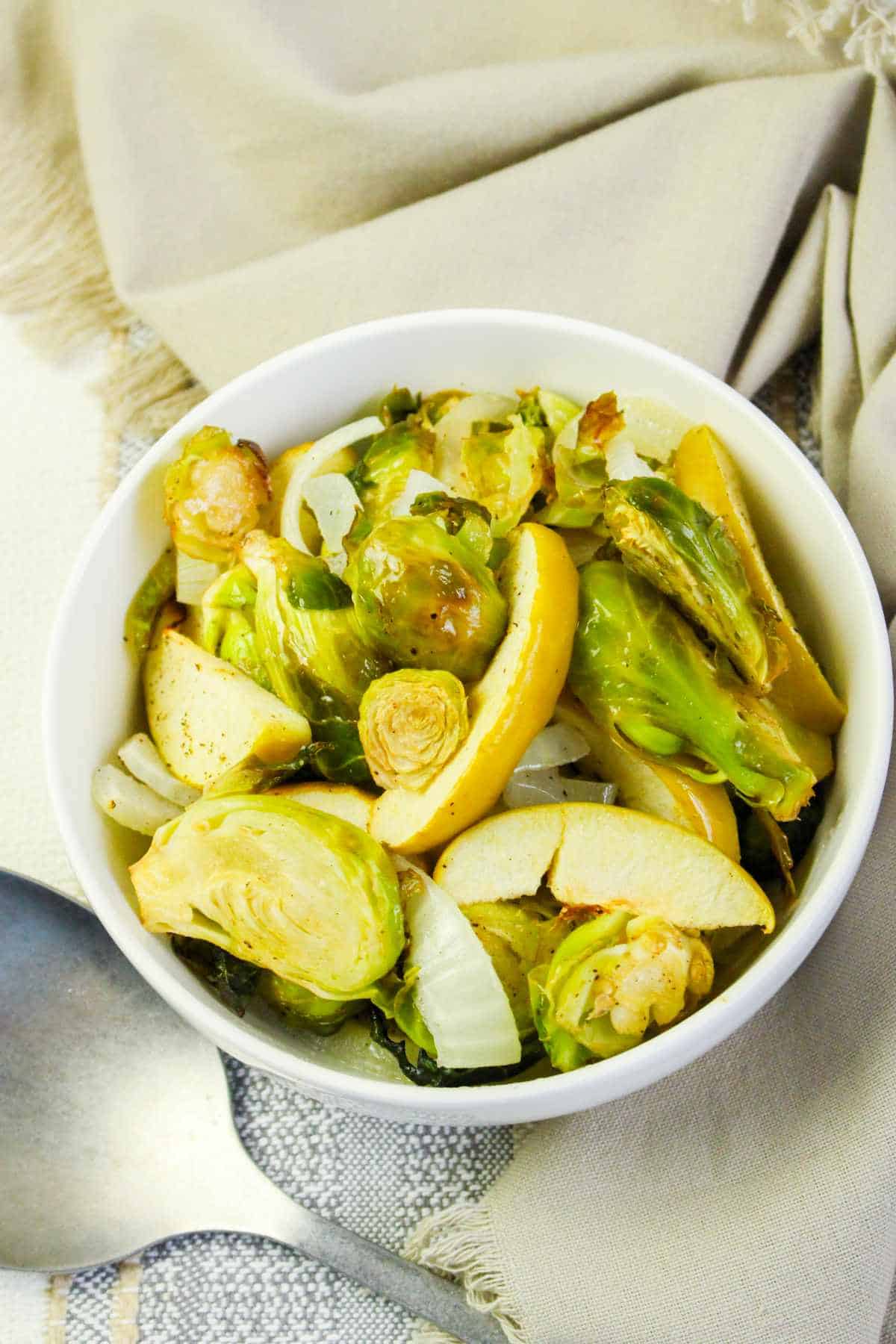 Serving bowl with roasted brussels sprouts and sliced granny smith apples.