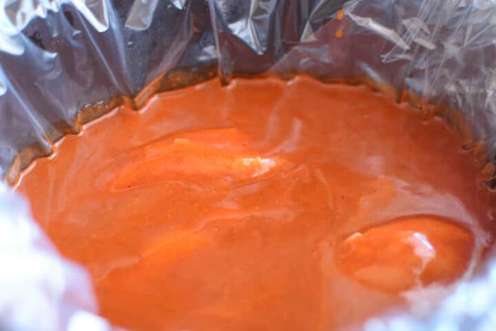Chicken breasts and red enchilada sauce in a lined slow cooker.
