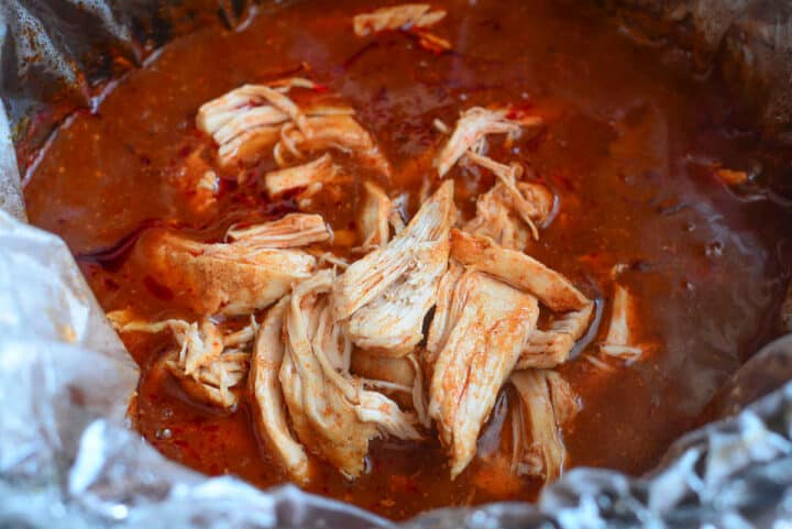 Shredded chicken mixed with red enchilada sauce in a slow cooker.