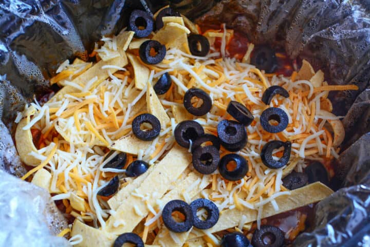 Chicken enchilada casserole mixture topped with shredded cheese and black olives in a slow cooker.