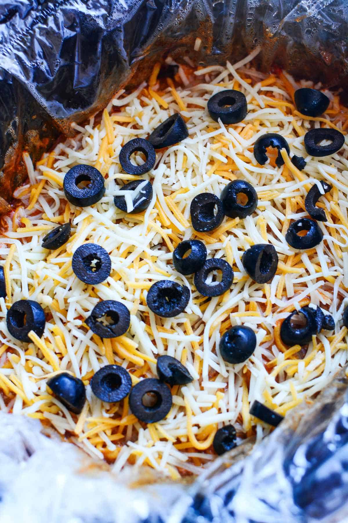 layers of tortilla strips, olives, and shredded cheese in a lined slow cooker