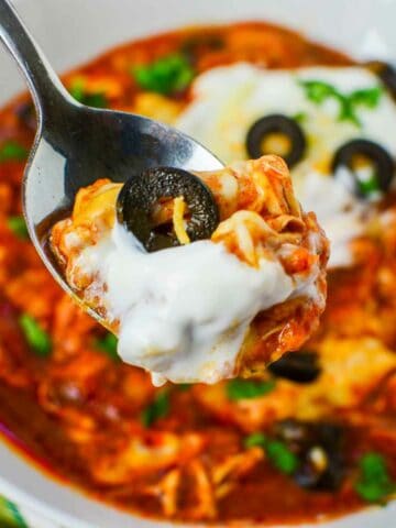 A spoonful of enchilada soup with sour cream, cheese, and black olives held above a bowl of more soup.