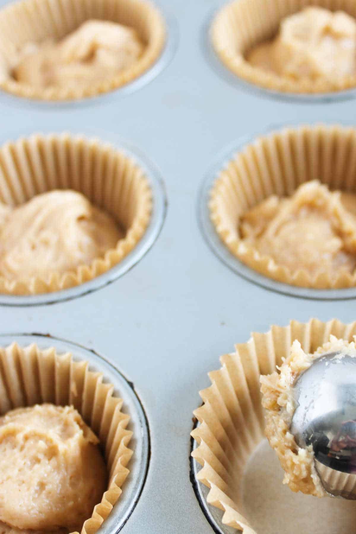 scoops of batter in lined muffin tin cavities.
