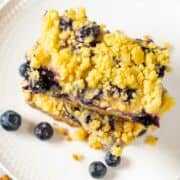 two blueberry lemon bars stacked on a plate.