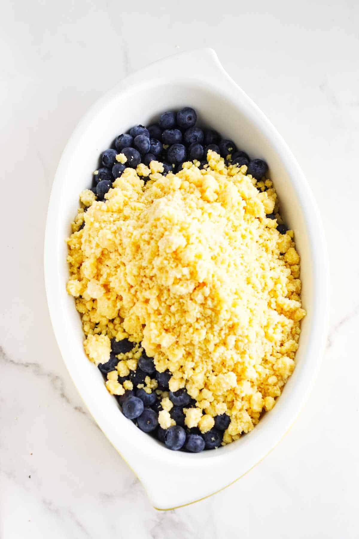 crumble mixture spread out on top of blueberries in a baking dish.