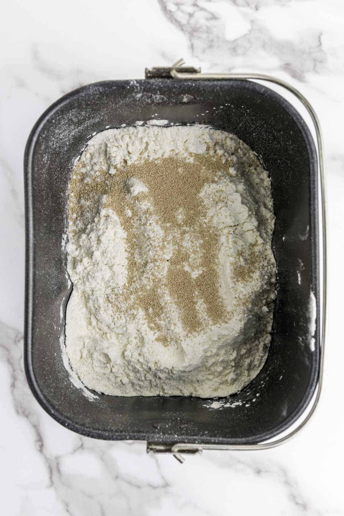 flour and yeast added to a bread machine baking pan.