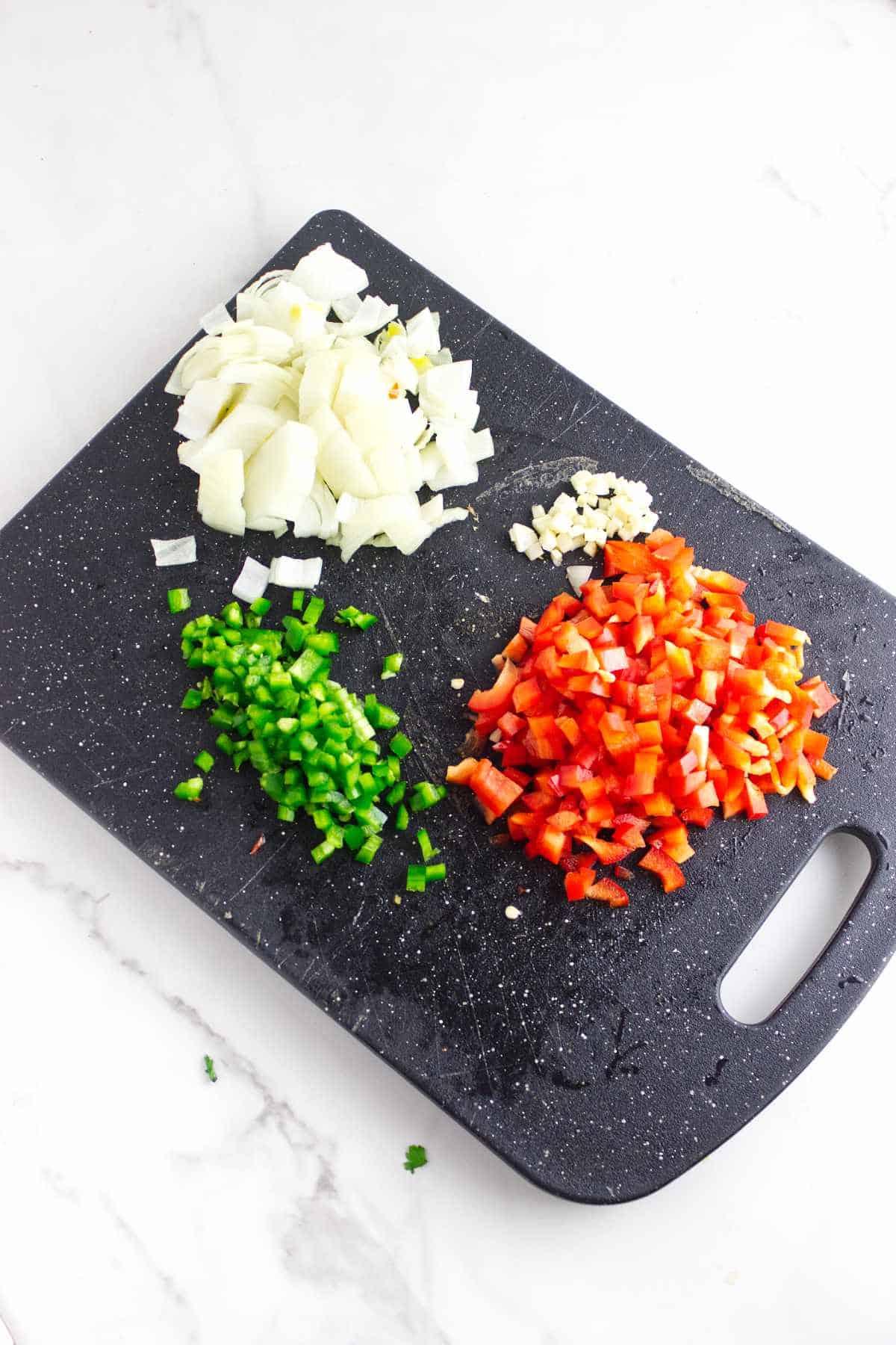 diced jalapeno, red bell pepper, and white onion on a cutting board.