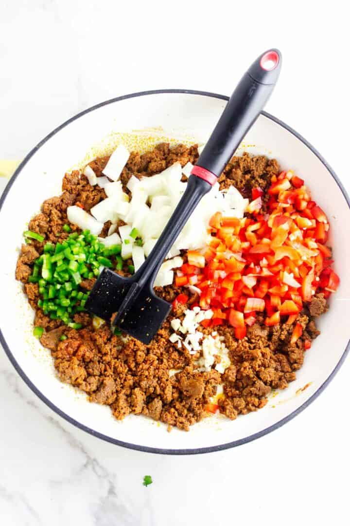Chorizo cooking with peppers and onions in a skillet.