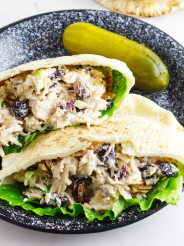 cranberry pecan chicken salad in pita pockets on a plate with a dill pickle.