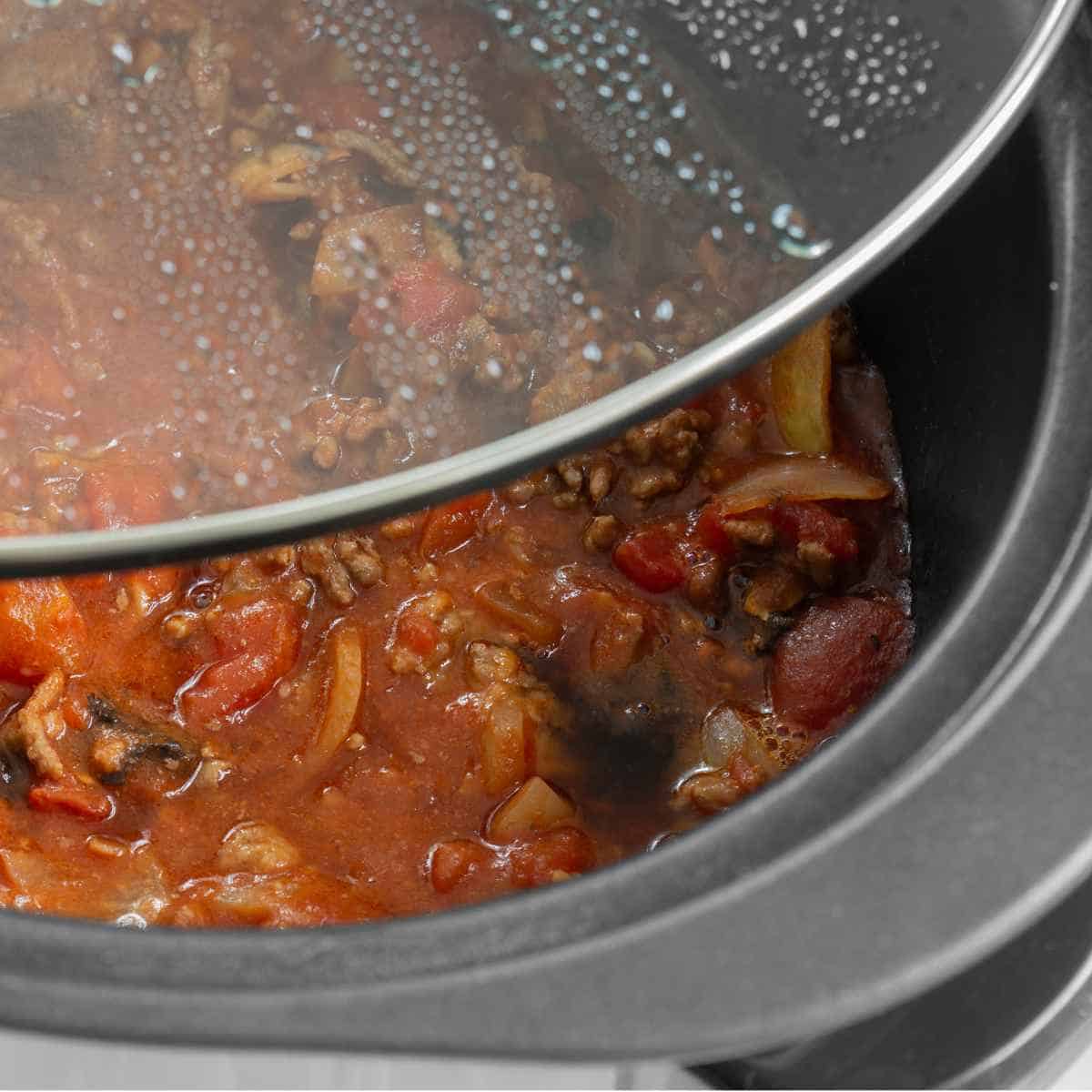 Bolognese sauce cooking in a slow cooker with glass lid lifted off. Perfect for Crocktober Fest.