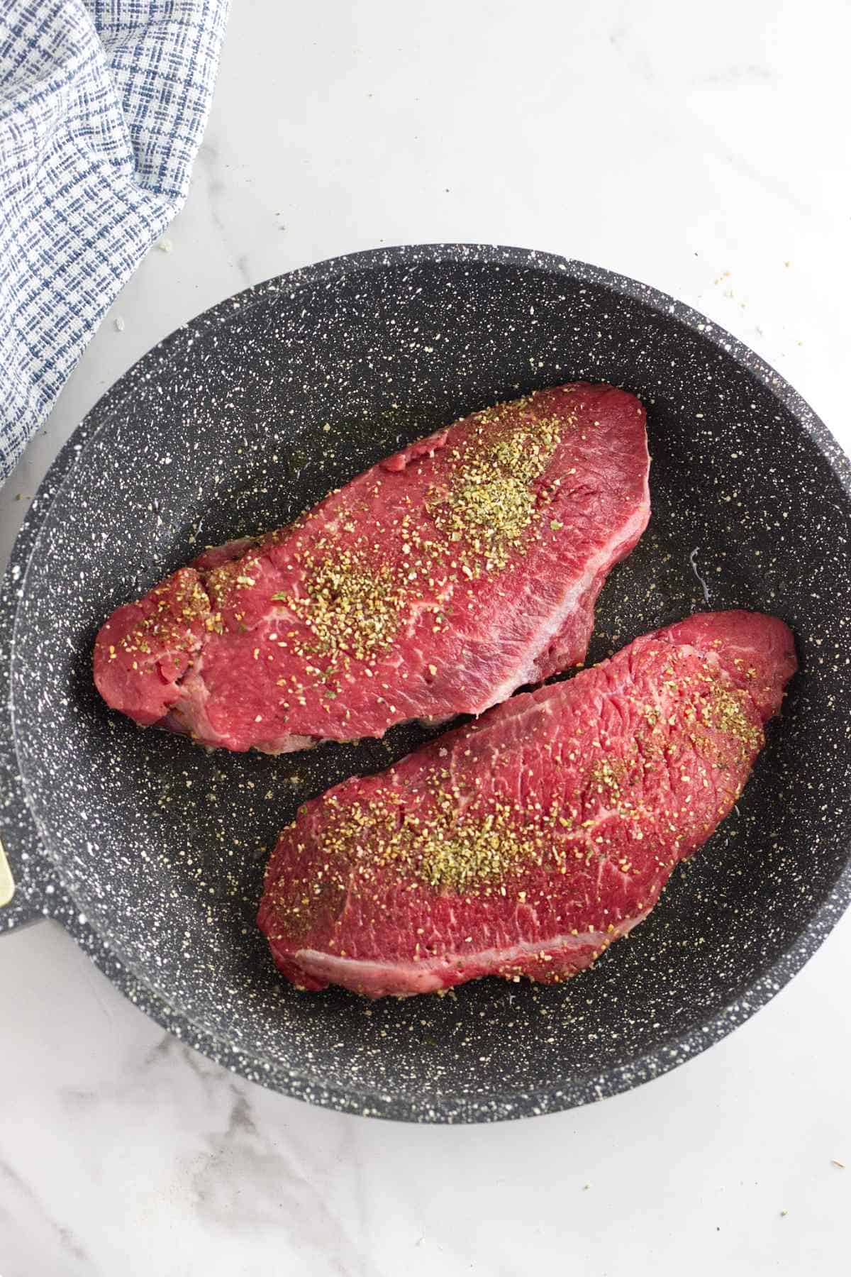 seasoned steaks sizzling in a skillet.