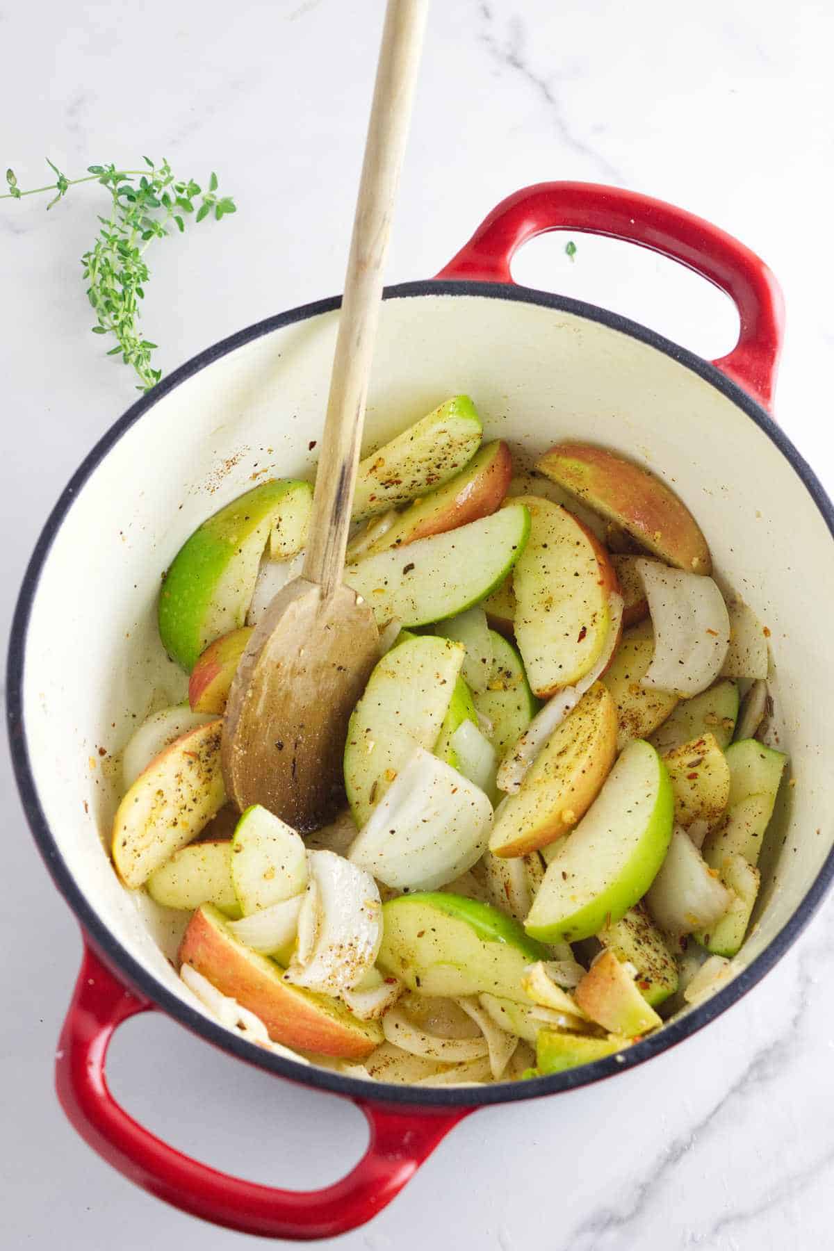 apples, onions, and garlic being sauteed in a pot.