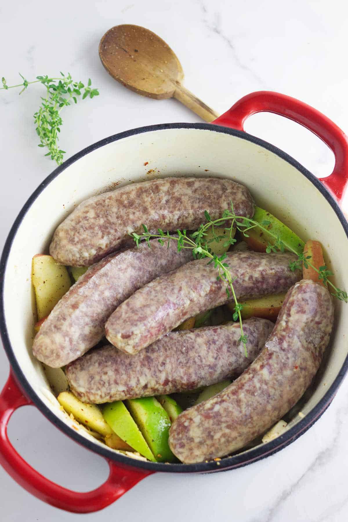 sausages added to a Dutch oven with sliced apples and onion.