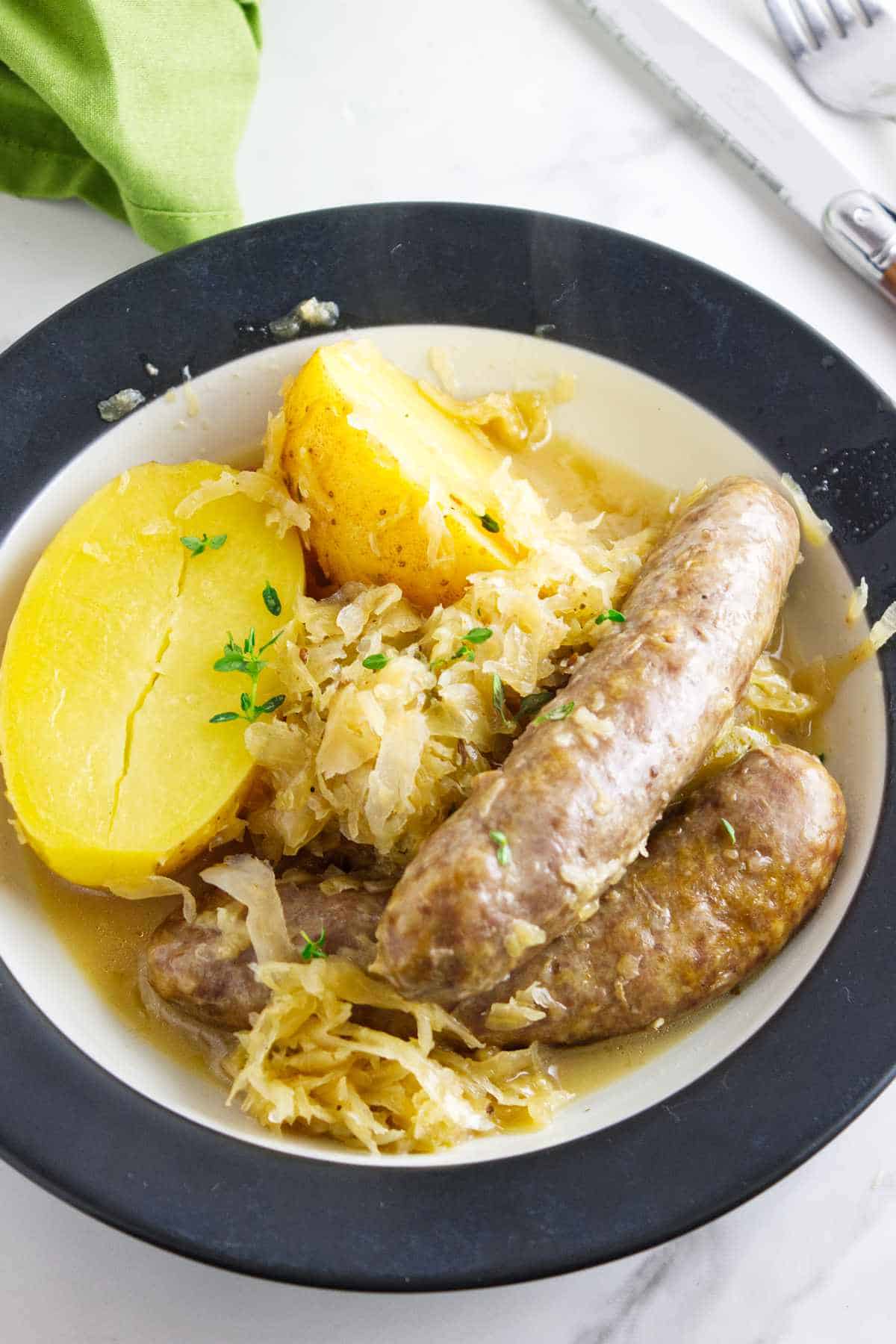 bowl holding a serving of bratwurst, potatoes, and sauerkraut.