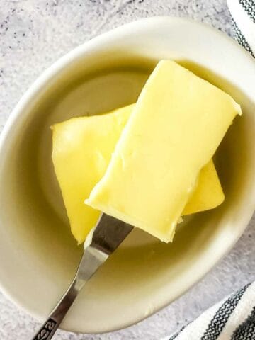 homemade butter in a crock with a butter knife holding a serving.