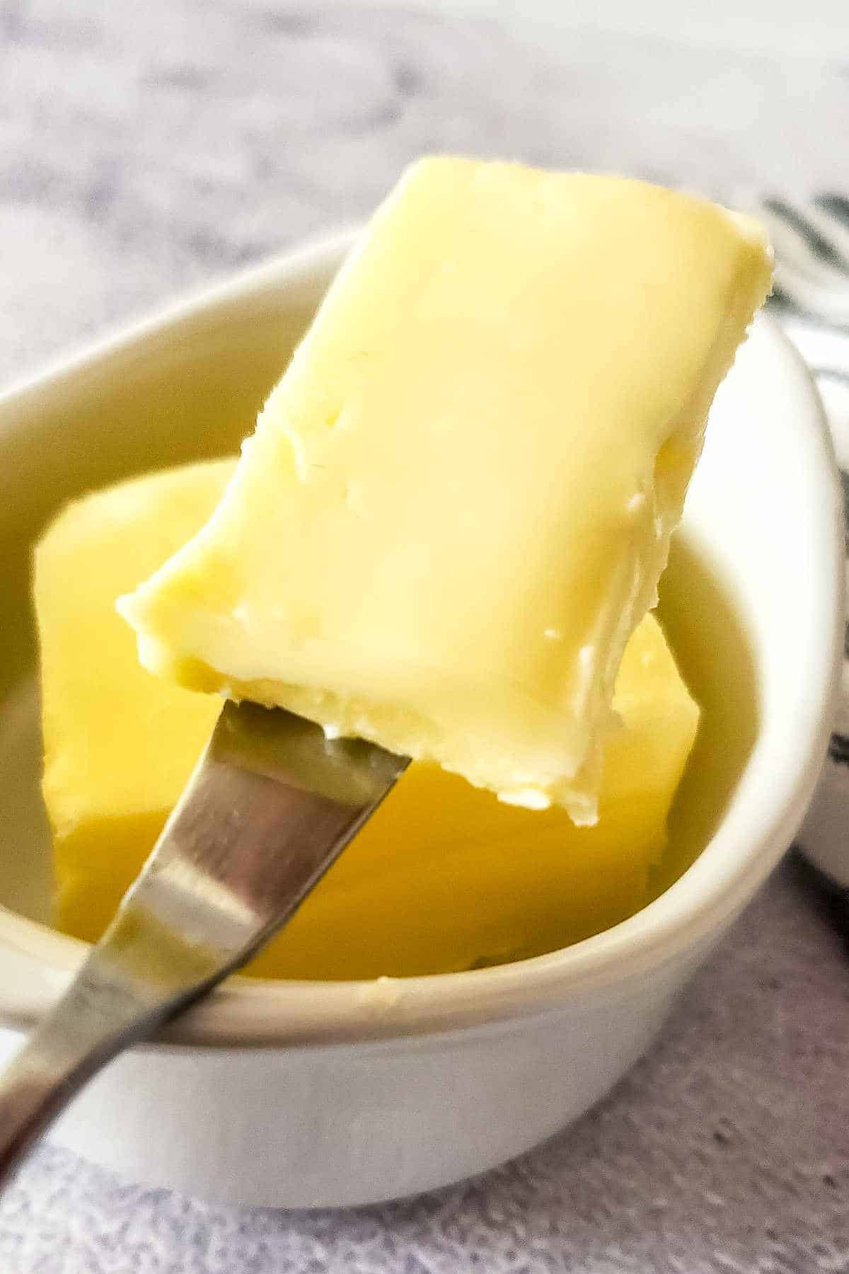 homemade butter in a crock with a butter knife holding a serving.