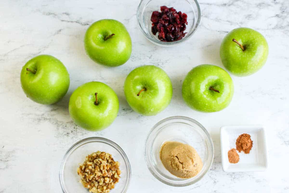 granny smith, dried fruit, nuts, brown sugar, and cinnamon in bowls on a white background.