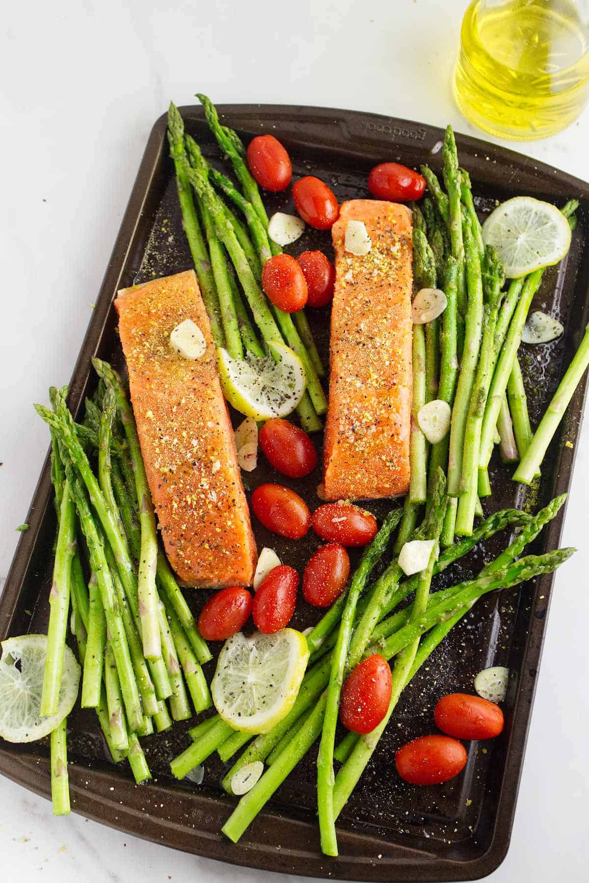 baking tray with raw seasoned asparagus spears, sliced lemons, and fish filets.