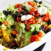 layered walking taco casserole with lettuce, tomato, sour cream, salsa, and olives on top.