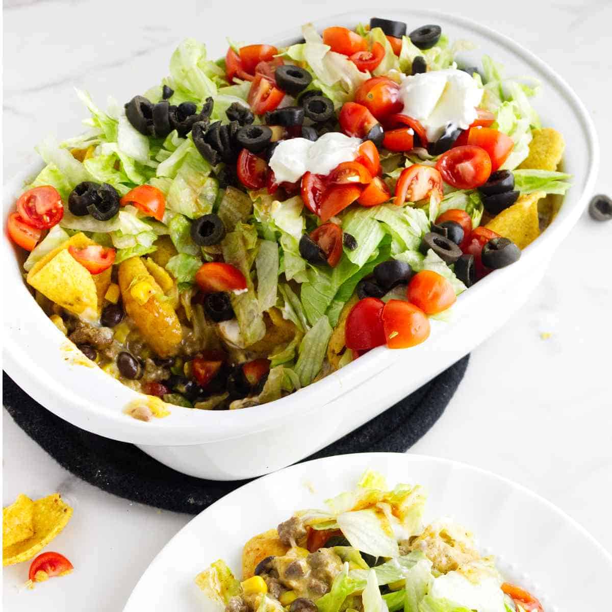 layered walking taco casserole with lettuce, tomato, sour cream, salsa, and olives on top.