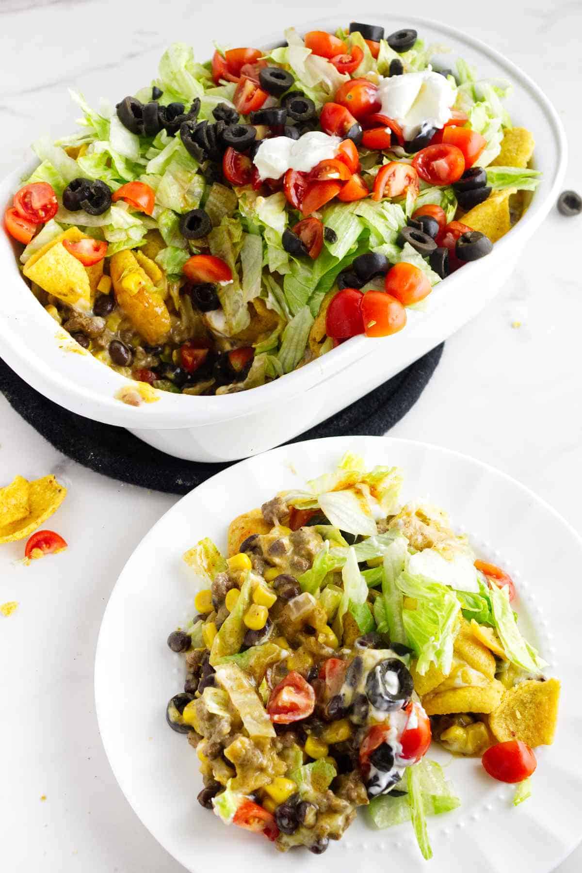 layered walking taco casserole with lettuce, tomato, sour cream, salsa, and olives on top.
